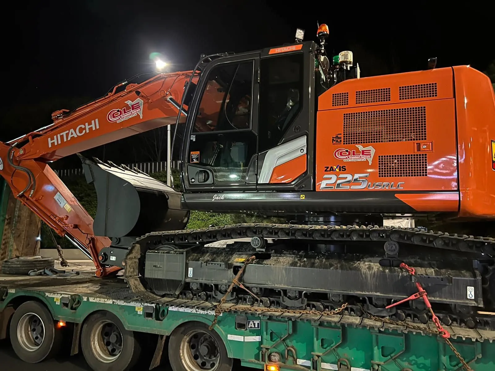 A Cole Hitachi excavator loaded on a low loader at night